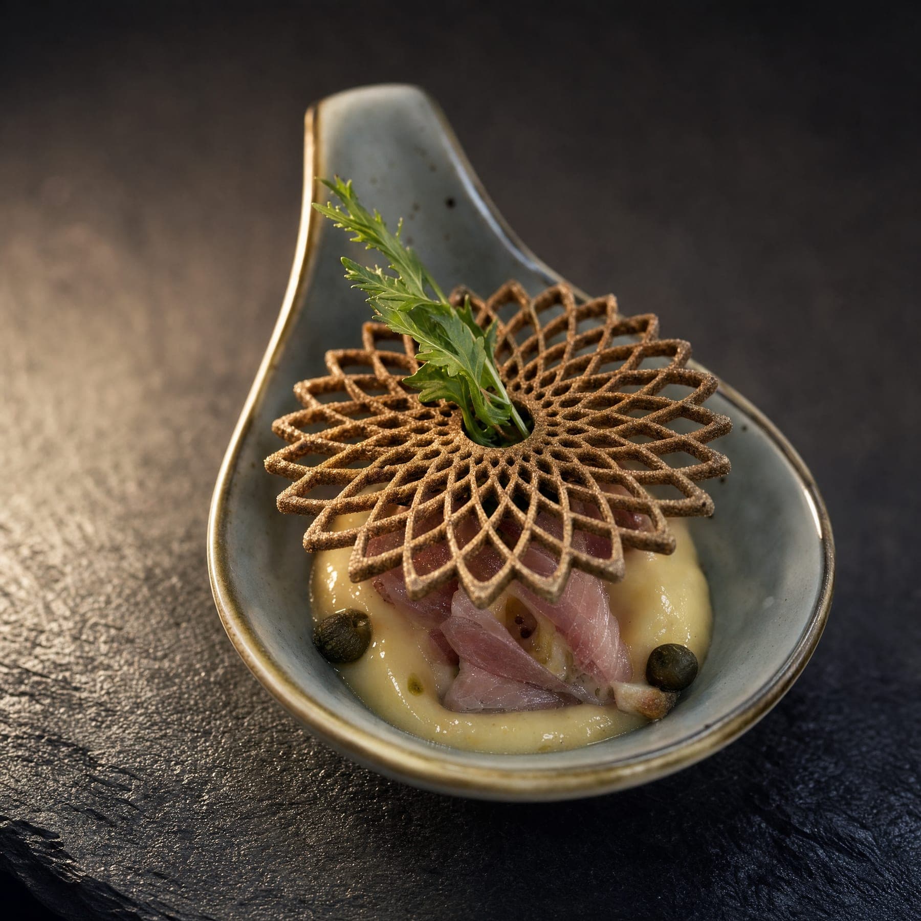 Amuse-Bouche auf einem Keramiklöffel mit gebackener Tuile und Kräuterspitze.